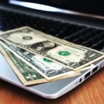 Close-up of US dollar bills placed on a laptop symbolizing digital finance and economy.make money online at home